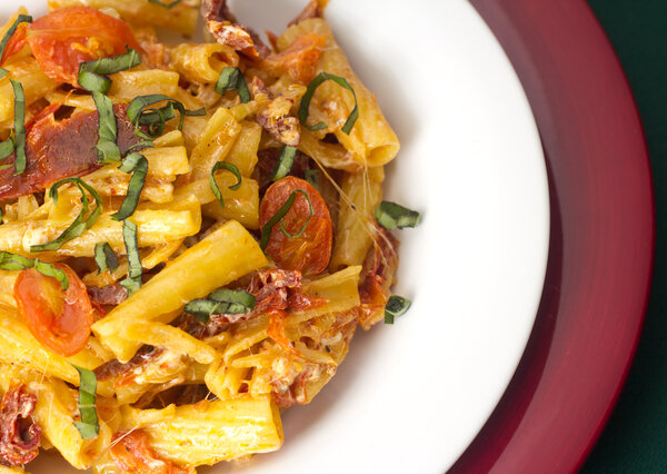 A serving of rigatoni mixed together with grape tomato halves, julienne cut sun dried tomatoes and gooey mozzarella cheese garnished with basil ribbons